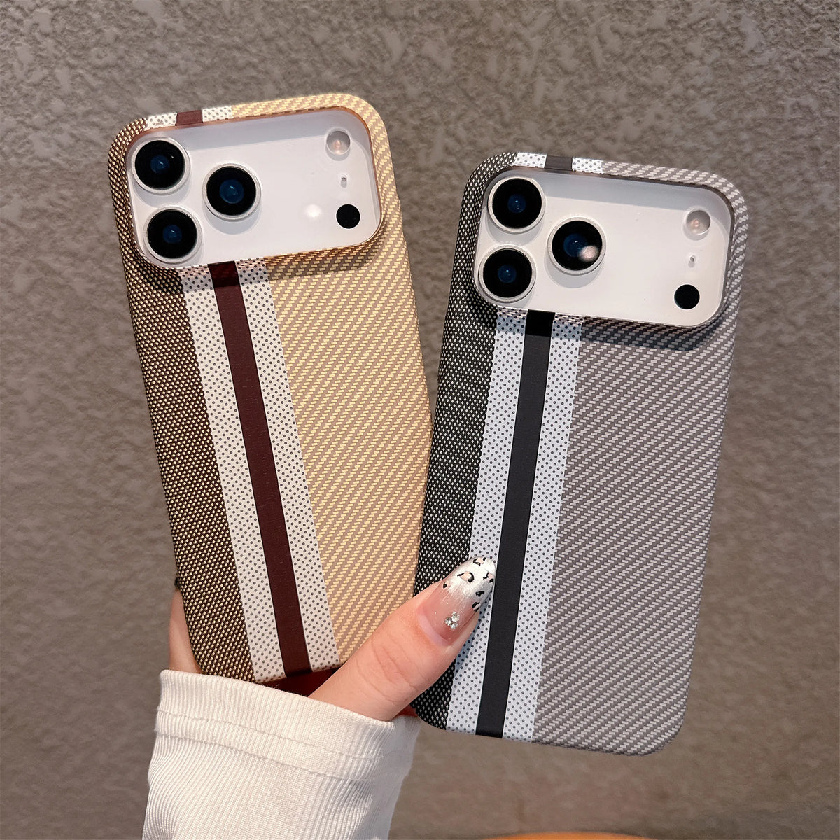 Two phone cases with striped patterns held by a hand against a brown background